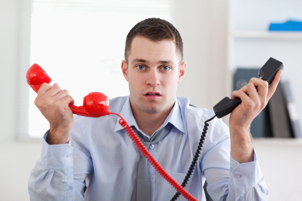 Man in office holding up two phones one red one black to show frustration at what he is listening to on both phones while waiting on-hold, on hold music or message importance  - on hold marketing concept