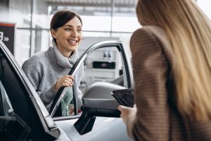 First impressions are crucial, and for many customers, their first interaction with your dealership could be through a phone call. On-hold marketing plays a pivotal role in setting this impression - car salesman speaking to smiling woman interested in car - successful marketing concept