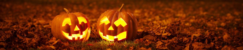 Two carved and lit jack-o-lantern pumpkins sitting in the grass on a dark night with an orange glow - halloween theme