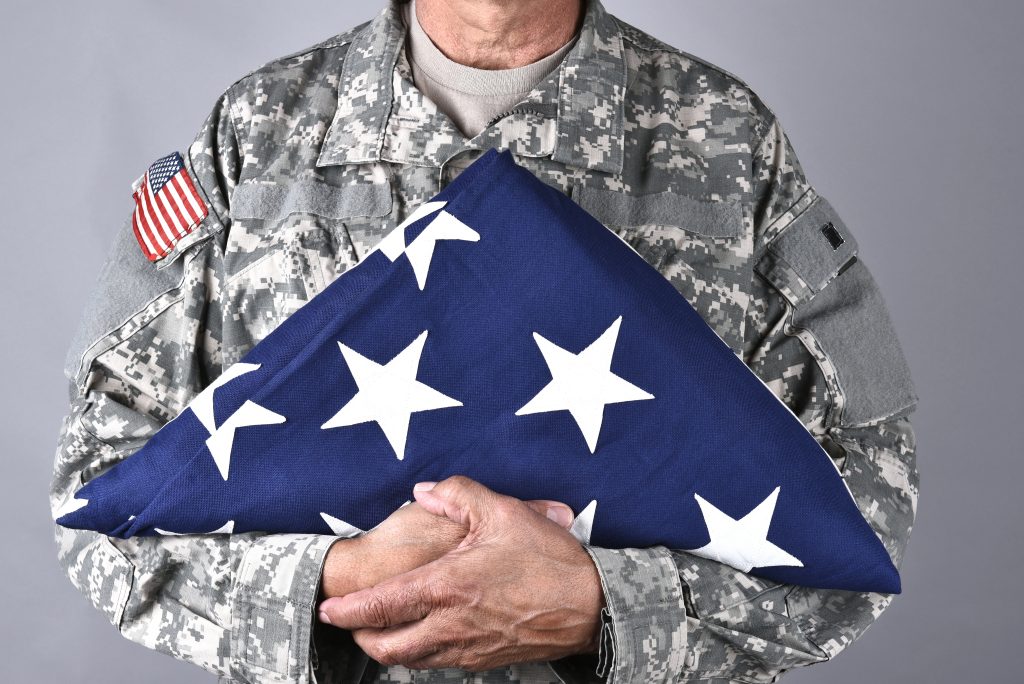 Closeup of an American Soldier in fatigues holding a folded flag in front of his torso - Implementing Veterans Day Recognition  