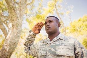 Proud soldier at attention, saluting; against a background of autumn trees - Veterans Day concept