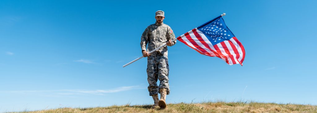 handsome soldier in uniform walking with american flag - As we approach Veterans Day, it's crucial for businesses to plan how they will honor this important day.