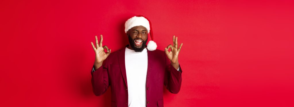 Industry-Specific Benefits of Professional Audio Services - Man in santa hat and red jacket holding up OK sign and winking in front of a red background