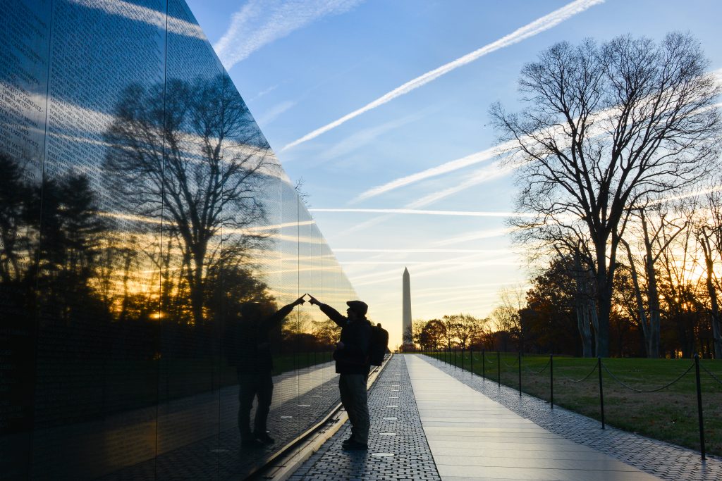 Washington DC - A Veteran looks for a name at Vietnam Veterans Memorial Wall at sunrise with the National Monument in the background