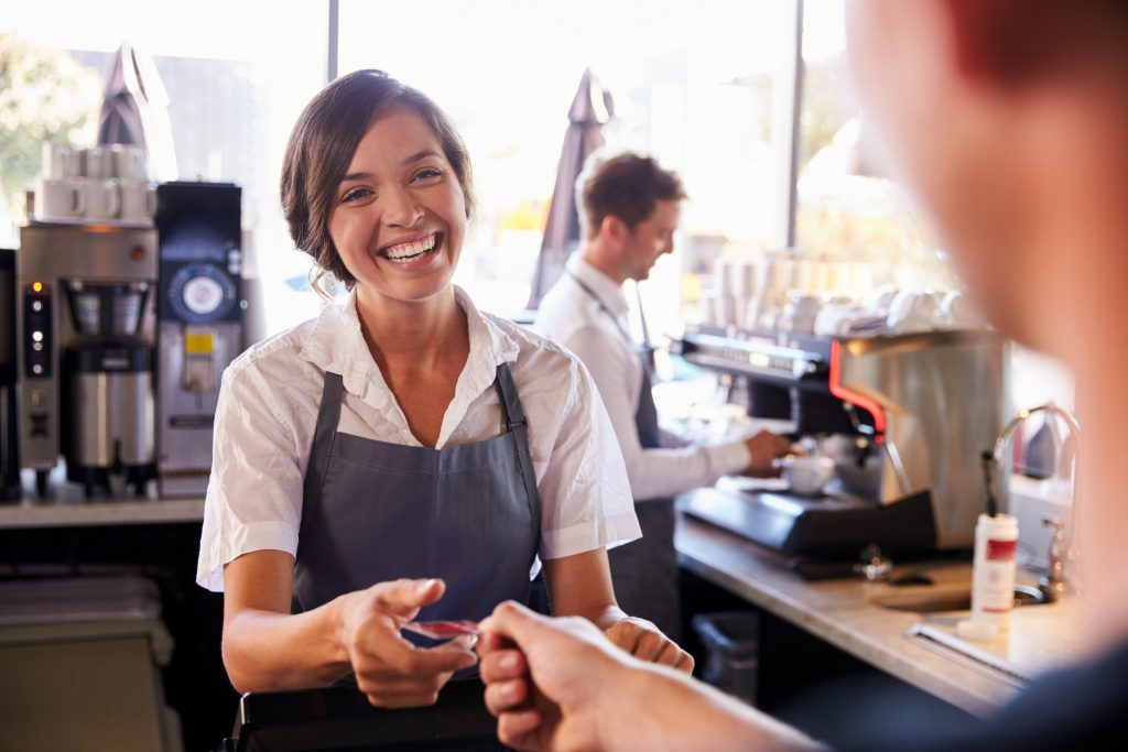 Utilizing Audio Branding to Meet Business Goals - Smiling barista takes card from paying customer in busy cafe