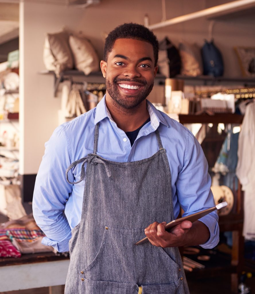 Smiling shop owner holding tablet wearing smock and looking at camera