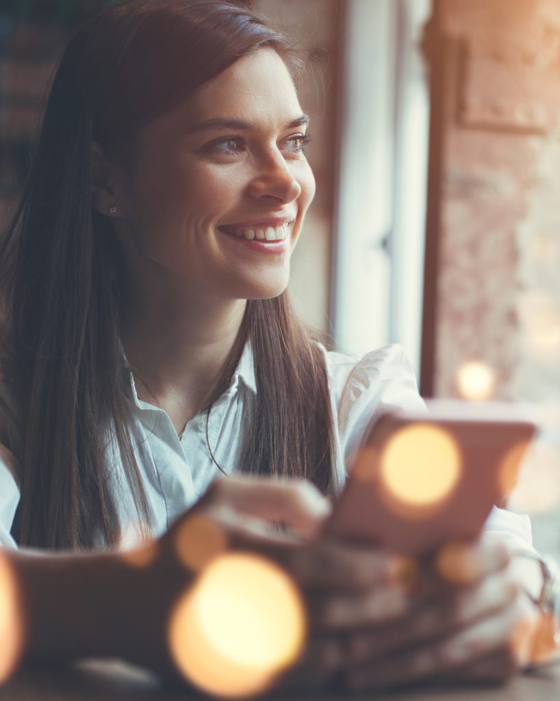 Smiling happy business woman holding cellphone looking out window