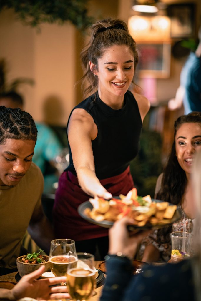 Maximizing Impact with Strategic Messaging - Waitress serving meals in a busy restaurant, smiling at happy guests receiving their food