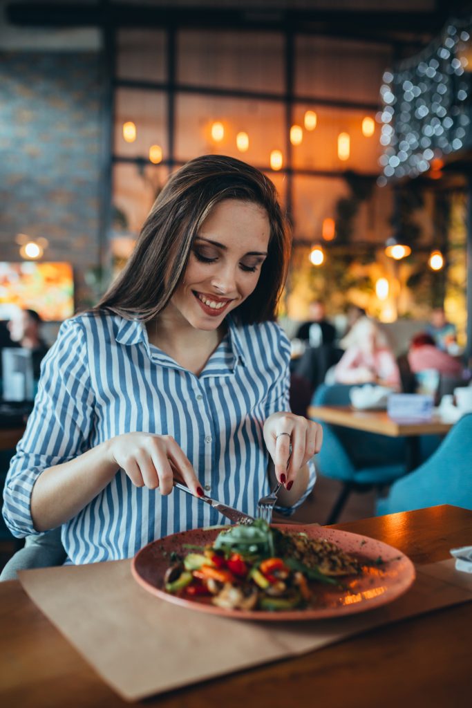 Enhancing Dining Ambiance with Overhead Music - Woman smiling and eating meal in a restaurant